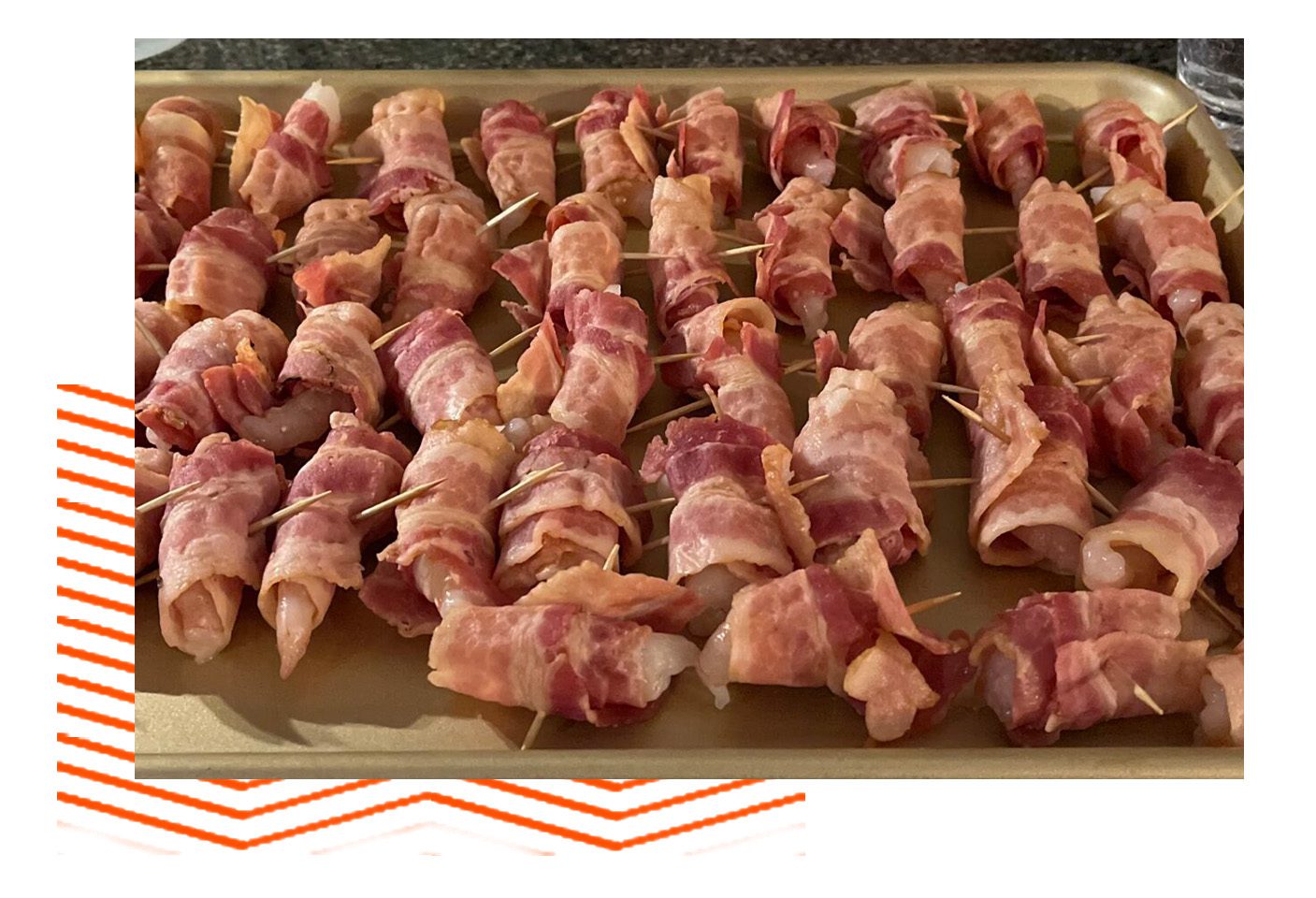 A tray of bacon wrapped meat on skewers.