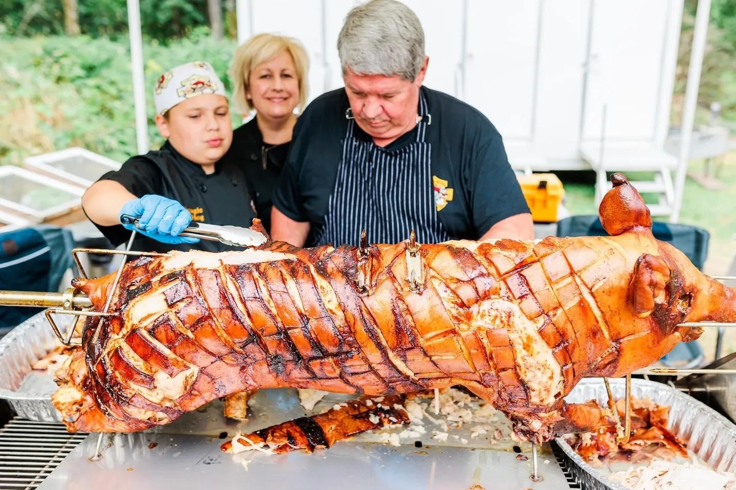 A man and two women standing over a large meat.